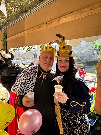 Helmut Peter und Christina Dost, verkleidet mit goldenen Kronen und pr&auml;chtigen Umh&auml;ngen, halten jeweils einen wei&szlig;en Becher und l&auml;cheln in die Kamera. Bunte Luftballons im Vordergrund.