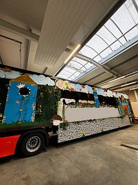 Seitliche Ansicht eines bunt bemalten Karnevalswagens in einer Halle, verziert mit Burgmotiven, Blumen und Wolken.