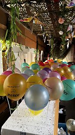 "Reihe bunter Luftballons mit der Aufschrift �Helau, Alaaf & Ahoi!� und dem Autohaus-Peter-Logo, befestigt an wei&szlig;en St&auml;ben, unter einer mit Pflanzen und Sternen dekorierten Decke.