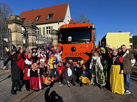 "Gruppe von kost&uuml;mierten Menschen in M&auml;rchen- und Tierverkleidungen posiert vor einem orangefarbenen LKW mit der Aufschrift �SCHADE�.