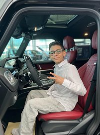 Jamil aus �The Voice Kids� sitzt auf dem Fahrersitz eines schwarzen Mercedes mit roter Lederausstattung, l&auml;chelt in die Kamera und zeigt ein Peace-Zeichen.