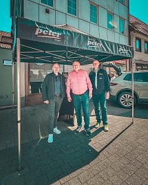 Drei M&auml;nner, darunter Gesch&auml;ftsf&uuml;hrer Helmut Peter, stehen unter einem schwarzen Pavillon mit Autohaus Peter-Logo in der Innenstadt.
