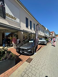 Zwei Mercedes-Ausstellungswagen, einer in Grau, einer in Silber, stehen vor einem Modegesch&auml;ft, Passanten schlendern vorbei.