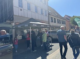 Menschen unterhalten sich unter einem schwarzen Autohaus Peter-Pavillon, daneben ein graues Ausstellungsfahrzeug.