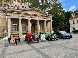 Oldtimeraufstellung vor Säulenfassade: Die gleichen vier Fahrzeuge sind vor dem klassizistischen Eingangsportal des Gebäudes in einer Reihe geparkt. Ein Aufsteller mit Veranstaltungsinfos steht vor dem grünen Cabrio.