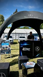 Infostand unter Pavillon: Mitarbeiter am schwarzen Mercedes-Benz Pavillon der Autohaus Peter Gruppe, im Vordergrund ein Aufsteller mit Stellenangeboten.