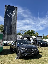 Mercedes-Benz SUV mit Flagge: Grauer Mercedes-Benz SUV vor schwarzer Mercedes-Flagge und Pavillon, weitere Fahrzeuge im Hintergrund.