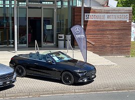 Ein schwarzes Mercedes-Benz Cabriolet steht vor der Stadthalle Wittenberg neben einer Mercedes-Fahne. Das Dach ist ge&ouml;ffnet, der Innenraum ist zu sehen.