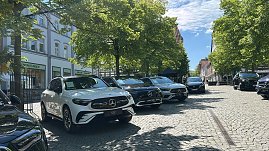 Mercedes-Benz Modellreihe: Verschiedene Mercedes-Benz Modelle, darunter SUVs und Limousinen, sind nebeneinander unter B&auml;umen auf einem gepflasterten Platz geparkt.