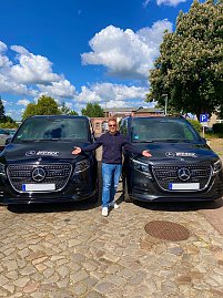 Daniel Kemp, Vorsitzender der Mukoviszidose Selbsthilfe e.V., steht mit ausgebreiteten Armen zwischen zwei schwarzen Mercedes-Benz Transportern mit Autohaus Peter-Logo.