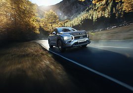 Fahrt durch die Berge: Silberner Mitsubishi Outlander fährt dynamisch auf einer kurvigen Bergstraße, umgeben von herbstlich gefärbten Bäumen.