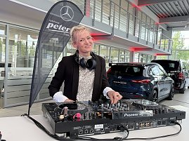 DJane mit Kopfhörern steht an einem Pioneer-DJ-Pult in einer Mercedes-Benz Ausstellungshalle und lächelt in die Kamera.