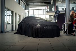 Ein Mercedes-Fahrzeug ist vollständig mit einem schwarzen Tuch bedeckt, auf dem Autohaus Peter steht, in einem hellen Ausstellungsraum.