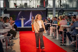 Eine Frau mit lockigem, blondem Haar, beiger Jacke, weißem Oberteil, Leopardenmuster-Hose und kleiner schwarzer Umhängetasche läuft über den roten Teppich.