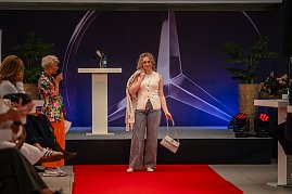 Eine blonde Frau mit Brille, ärmellosem cremefarbenem Oberteil, gemusterten Hosen und passender Handtasche präsentiert sich am Ende des roten Teppichs.