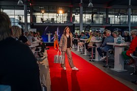 Frau im beigefarbenen Hosenanzug mit braunem Oberteil und großem, silberfarbenem Shopper läuft auf dem roten Teppich.