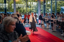 Frau mit kurzem blondem Haar, weißer Jacke und langem, dunkelblauem Kleid mit weißen Punkten läuft über den roten Teppich.