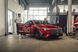 Roter Mercedes-Benz CLA 250+ mit Aufschrift She’s Mercedes auf der Fahrertür, zwei Männer stehen daneben in einer Ausstellungshalle. Mercedes-Benz CLA 250+ mit EQ-Technologie | Energieverbrauch kombiniert: 14,1-12,2 kWh/100 km | CO2Emissionen kombiniert: 0 g/km | CO2-Emissionsklasse: A