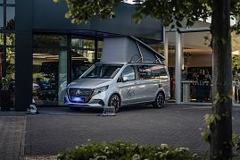 Silberner Mercedes-Van mit She’s Mercedes-Logo, vor einem Autohaus geparkt, mit geöffnetem Aufstelldach wie bei einem Camper.