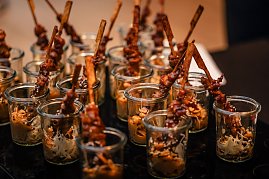 Mehrere kleine Gläser gefüllt mit asiatisch anmutenden Snacks, darin marinierte Fleischspieße mit Sesam und Beilage.