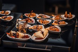 Kleine weiße Schälchen und Gläser mit Fingerfood, darunter Fleischspieße, Frühlingsrollen und Nudeln, appetitlich angerichtet.