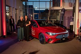 Zwei Frauen, darunter Christina Dost, posieren neben einem roten Mercedes mit She’s Mercedes-Logo, im Hintergrund eine Treppe und weitere Gäste.