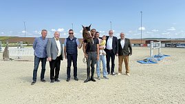 Pressekonferenz auf dem Reitplatz in Immenrode: Sieben erwachsene Personen stehen nebeneinander, darunter ein Reiter mit Pferd und eine Person mit Kind auf dem Arm. Im Hintergrund sind Hindernisse und die Reitplatzanlage zu sehen. Die Veranstaltung dient der offiziellen Vorstellung des Reitturniers Immenrode 2025.