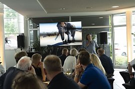 Abenteuer-Guide Hannu pr&auml;sentiert beim s&uuml;dafrikanischen Abend im Autohaus Peter in Heiligenstadt spannende Eindr&uuml;cke einer Safari, w&auml;hrend auf dem Bildschirm ein Elefant zu sehen ist und die G&auml;ste aufmerksam zuh&ouml;ren.