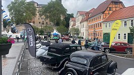 Blick auf eine Oldtimerschau in der Altstadt von Sondershausen. Mehrere historische Fahrzeuge sind auf dem Kopfsteinpflaster ausgestellt. Im Vordergrund klassische Mercedes- und Opel-Modelle, daneben Beachflags mit den Logos von Mercedes-Benz, Opel und Autohaus Peter. Im Hintergrund Fachwerkhäuser und das Schloss Sondershausen. Besucher schlendern durch die Ausstellung.