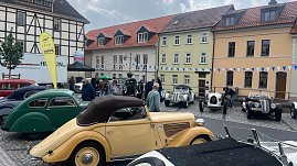 Mehrere Oldtimer stehen auf dem Marktplatz von Sondershausen vor einer Häuserzeile mit bunten Fassaden. Zu sehen sind historische Fahrzeuge in verschiedenen Farben und Karosserieformen – unter anderem ein cremefarbenes Cabriolet im Vordergrund. Menschen schlendern zwischen den Autos.