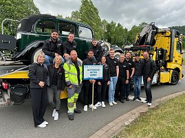 Gruppenfoto eines Teams des Autohaus Peter beim Festumzug in Sondershausen. Die Mitarbeitenden stehen vor einem klassischen Abschleppwagen des ADAC mit einem Oldtimer auf der Ladefläche. Alle tragen schwarze Autohaus-Peter-Bekleidung, einige lachen in die Kamera. Im Vordergrund wird ein Schild mit der Aufschrift Autohaus Peter GmbH gehalten. Im Hintergrund Bäume und bewölkter Himmel.
