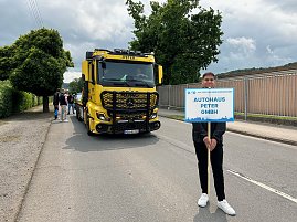 Ein junger Mann steht auf einer Straße und hält ein Schild mit der Aufschrift Autohaus Peter GmbH bei einem Festumzug in Sondershausen anlässlich 900 Jahre Sondershausen. Hinter ihm steht ein gelber Mercedes-Benz Abschlepp-Lkw mit der Aufschrift Peter auf der Windschutzscheibe. Weitere Personen und Fahrzeuge sind im Hintergrund zu sehen.