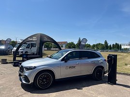 Ein silberner Mercedes-Benz SUV mit Autohaus-Peter-Logo steht bei einer Präsentation im Freien am Ladegerät. Im Hintergrund sind ein schwarzes Zelt mit der Aufschrift ‚Jetzt Probe fahren‘, Fahnen und weitere Fahrzeuge zu sehen. Die Szene gehört zum Leichtathletik-Meeting Anhalt 2025.