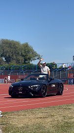 Ein schwarzes Mercedes-Benz Cabrio des Autohauses Peter fährt über die rote Laufbahn beim Leichtathletik-Meeting Anhalt 2025. Ein Sportler winkt den Zuschauern auf der Tribüne vom Cabrio aus zu.