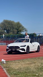 Ein weißes Mercedes-Benz Cabrio des Autohauses Peter fährt über die rote Laufbahn beim Leichtathletik-Meeting Anhalt 2025. Ein Sportler sitzt darin; im Hintergrund sind Zuschauertribünen und Bäume zu sehen.