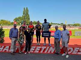 Siegerehrung beim Leichtathletik-Meeting Anhalt 2025: Sportlerinnen und Sportler stehen auf dem Podium mit Blumen in der Hand, einer hält ein Schild mit der Aufschrift ‚Meeting Rekord‘. Vor dem Podium posieren mehrere Erwachsene, im Hintergrund sind Laufbahn und Zuschauertribünen.