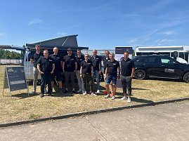 Gruppenfoto des Teams vom Autohaus Peter bei sonnigem Wetter. Zehn Personen stehen in schwarzer Teamkleidung mit Logo ‚Peter‘ nebeneinander vor einem silbernen Van und einem schwarzen Mercedes. Im Hintergrund sind ein Zelt, Werbebanner und weitere Fahrzeuge zu sehen. Alle lächeln in die Kamera.