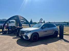 Ein silberner Mercedes-Benz SUV des Autohauses Peter steht während des Leichtathletik-Meetings Anhalt 2025 an einer mobilen Ladesäule. Links befindet sich ein schwarzes Promotion-Zelt mit dem Schriftzug ‚Jetzt Probe fahren‘, daneben mehrere Boxen und Mitarbeiter des Autohauses. Im Hintergrund sind Wohnmobile, Bäume und ein sonniger, klarer Himmel zu sehen.