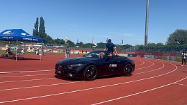 Ein schwarzes Mercedes-AMG Cabrio des Autohauses Peter fährt mit einem Sportler über die Laufbahn im Stadion des Anhalt 2025 Leichtathletik-Meetings. Im Hintergrund sind das blaue Zelt der Stadtwerke Dessau, einige Zuschauer und die Beschilderung mit ‚WELCOME‘ und ‚BIENVENUE‘ zu sehen.
