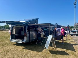 Auf dem Außengelände des Anhalt 2025 Leichtathletik-Meetings stehen mehrere Mercedes-Benz Fahrzeuge des Autohauses Peter, darunter ein silberner Campingbus mit geöffneten Türen und ausgefahrenem Aufstelldach. Menschen informieren sich an Infoständen unter Sonnenschein, während im Hintergrund weitere Fahrzeuge und Besucher zu sehen sind.