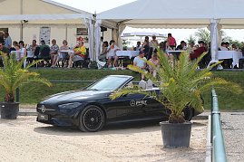 Ein schwarzes Mercedes-Benz Cabrio steht am Rand des Sandplatzes beim Reitturnier in Immenrode, flankiert von zwei Palmen im Topf. Im Hintergrund sitzen Zuschauer unter wei&szlig;en Eventzelten an Tischen.