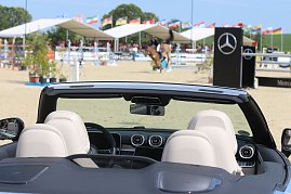 Blick &uuml;ber die Sitze eines schwarzen Mercedes-Benz Cabrios auf den Springplatz beim Reitturnier in Immenrode. Im Hintergrund springt ein Reiter &uuml;ber ein Hindernis, flankiert von Mercedes-Benz-Werbebannern und zahlreichen L&auml;nderflaggen.