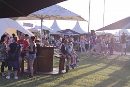 Besucher genie&szlig;en den Abend auf der Wiese beim Reitturnier in Immenrode. Unter gro&szlig;en Sonnenschirmen und Pagodenzelten stehen Gruppen zusammen, einige G&auml;ste sitzen an Stehtischen oder auf B&auml;nken.