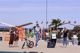 Siegerehrung beim Reitturnier in Immenrode: Auf dem Sandplatz stehen f&uuml;nf Erwachsene, einer spricht ins Mikrofon. Vor ihnen liegen Preise wie ein Kinderfahrrad und Geschenktaschen, im Hintergrund sitzen Zuschauer auf den Trib&uuml;nen unter wehenden Fahnen.