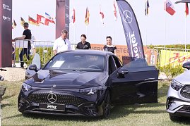 Ein schwarzes Mercedes-Benz Fahrzeug steht mit ge&ouml;ffneter Fahrert&uuml;r auf der Ausstellungsfl&auml;che beim Reitturnier in Immenrode. Dahinter stehen drei Erwachsene, im Hintergrund sind Fahnen, Absperrgitter und ein Werbebanner des Autohauses Peter zu sehen.
