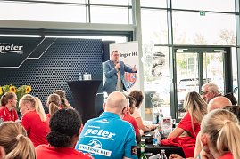 Bodo Ramelow spricht beim Medien-Tag des Thüringer HC in Erfurt. Er steht mit Mikrofon in der Hand an einem Stehtisch vor einem Publikum aus Spielerinnen und Gästen, die überwiegend rote Shirts tragen. Im Hintergrund Banner mit dem Logo des Thüringer HC.