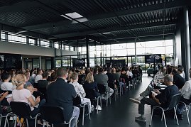 Blick von hinten in die Veranstaltungshalle: Zahlreiche Auszubildende und ihre Eltern sitzen in Reihen und verfolgen die Begr&uuml;&szlig;ung der Autohaus-Peter-Gruppe.