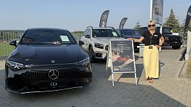 Eine Frau mit schwarzem Polohemd, gelber Hose und Sonnenbrille steht neben einem Aufsteller mit Werbung für den neuen Mercedes CLA. Links im Bild ein schwarzer Mercedes CLA, daneben weitere Mercedes-Modelle in Weiß und Schwarz. Im Hintergrund wehen schwarze Fahnen mit Mercedes-Logo. Aufnahme beim Leichtathletikmeeting in Sondershausen.