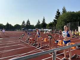 Mehrere Athletinnen bereiten sich auf der Tartanbahn an den Startblöcken vor. Einige gehen bereits in die Hocke, andere stehen noch. Zuschauer im Hintergrund.