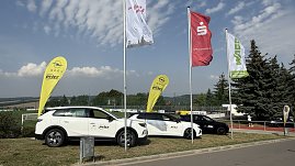 Zwei weiße und ein schwarzes Opel-Fahrzeug vom Autohaus Peter stehen nebeneinander auf dem Rasen auf dem Weg zum Stadion. Daneben gelbe Opel-Werbebanner sowie Fahnen der Kyffhäusersparkasse, WAGO und weiterer Sponsoren.